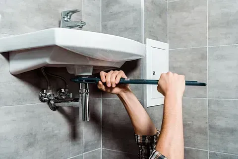 Fontanero utilizando una llave inglesa para trabajar en las tuberías debajo del lavabo del baño.