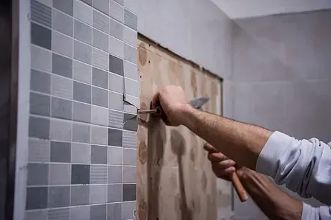Persona quitando azulejos de la pared con un cincel y un martillo.