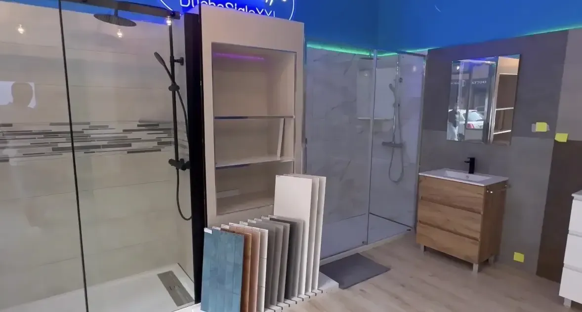 Sala de exposición de baños con duchas de muestra, tocador, muestras de azulejos y paredes azules/grises.