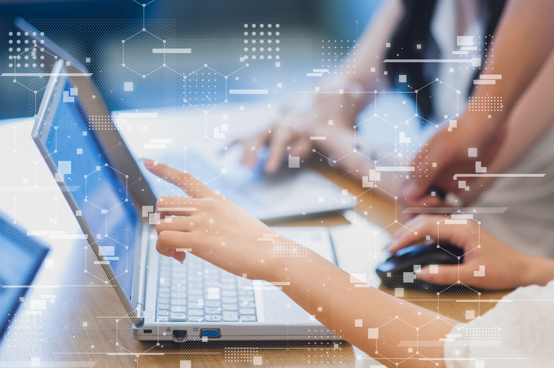 Deux personnes travaillent sur des ordinateurs portables, l'une pointant du doigt l'écran sur lequel sont superposés des schémas de circuits numériques.