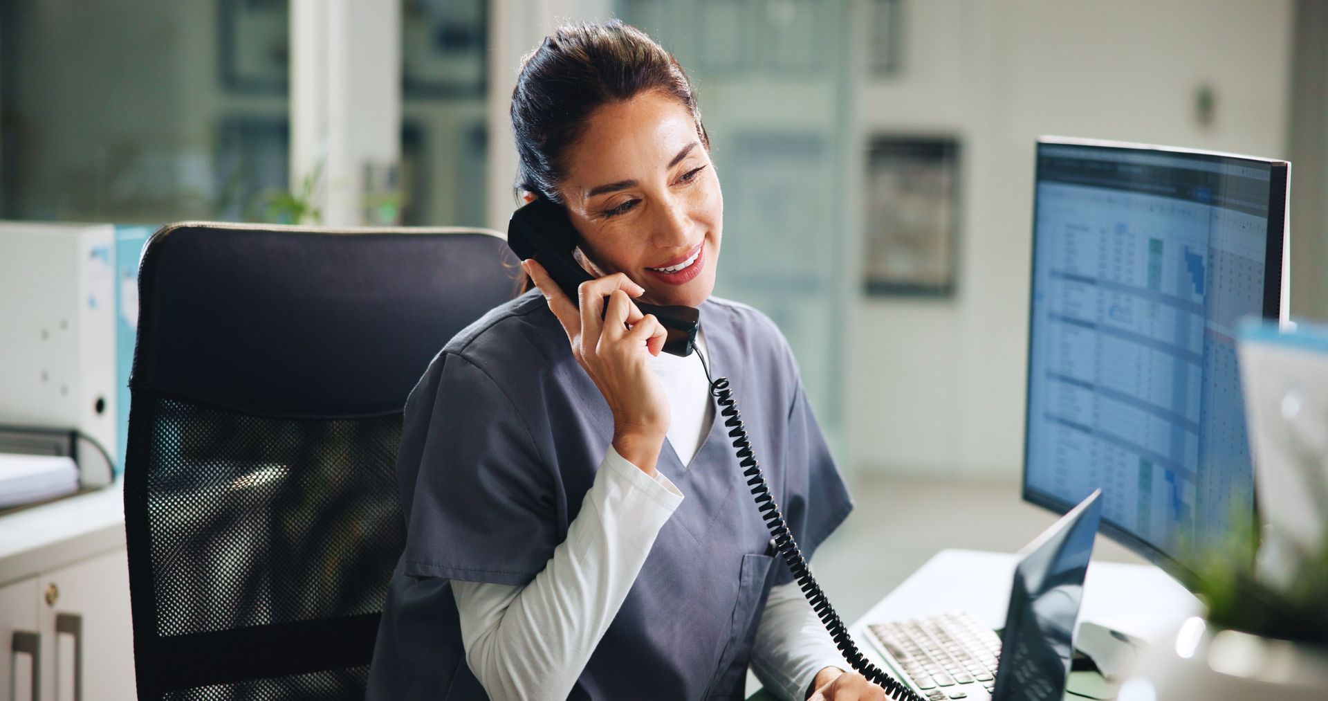 Professionnel de santé au téléphone, souriant à son bureau devant son ordinateur.
