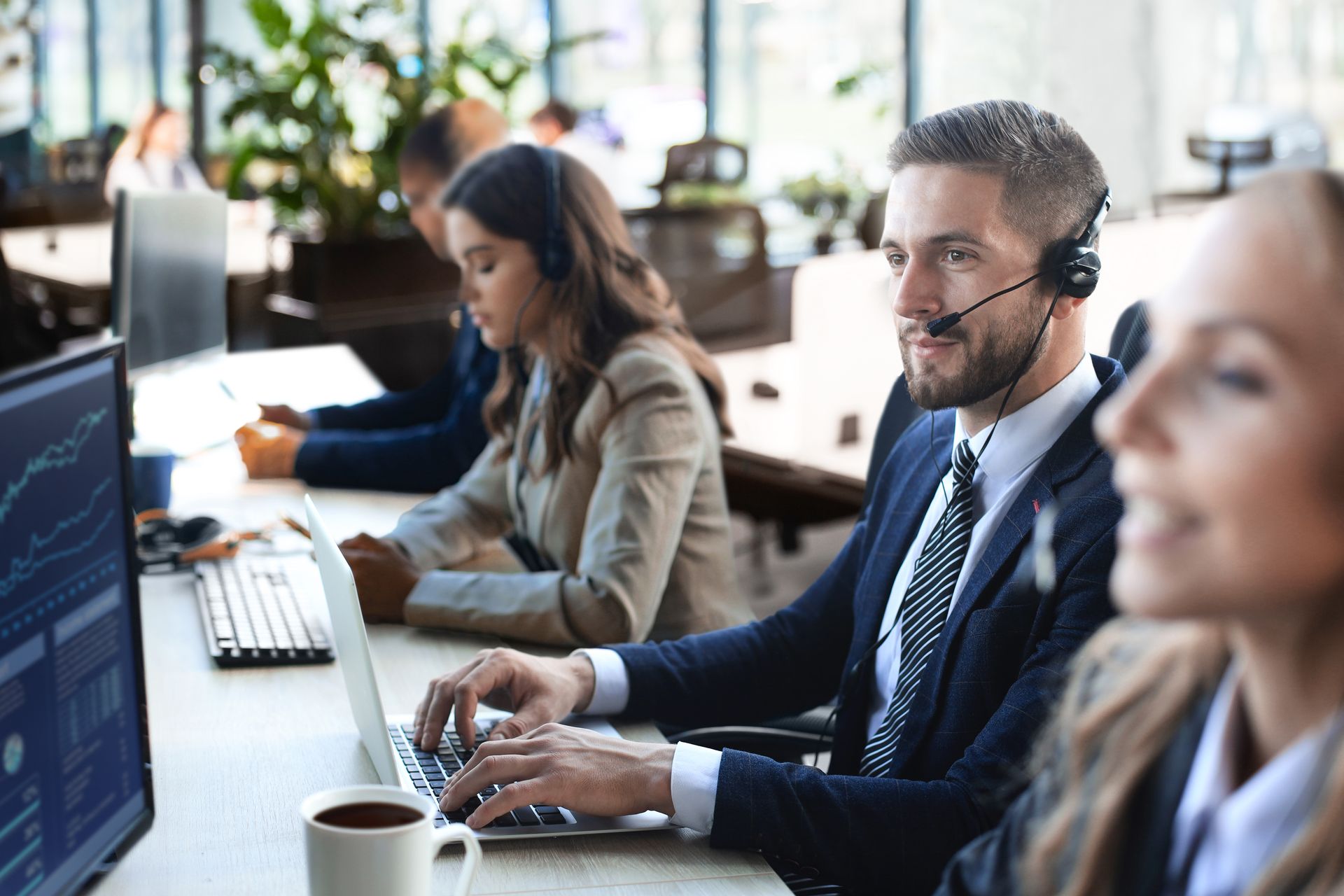 Des personnes en costume, portant des casques audio, travaillent sur des ordinateurs dans un bureau.