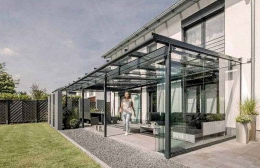 Una mujer camina bajo un dosel de vidrio frente a una casa.
