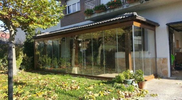 Una gran habitación de cristal con puertas corredizas de cristal se encuentra en el patio trasero de una casa.