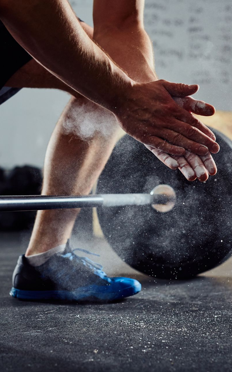 Un homme frappe des mains couvertes de craie au-dessus d'un poids dans une salle de sport.
