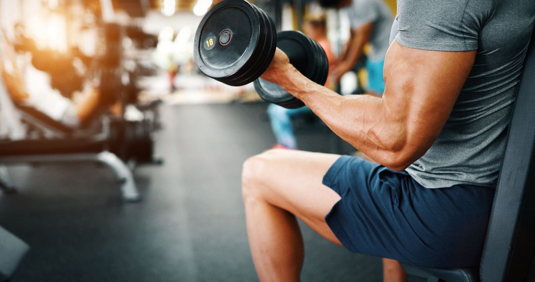Homme assis, soulevant un haltère dans une salle de sport.
