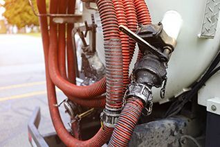 Rote Schläuche sind mit einem weißen Tank auf einem LKW verbunden, ein schwarzes Ventil ist sichtbar.