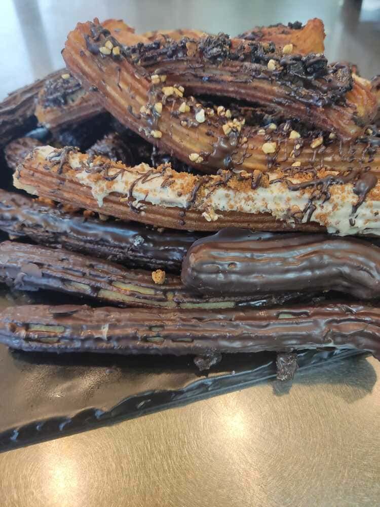 Una pila de churros cubiertos de chocolate con nueces sobre una mesa.