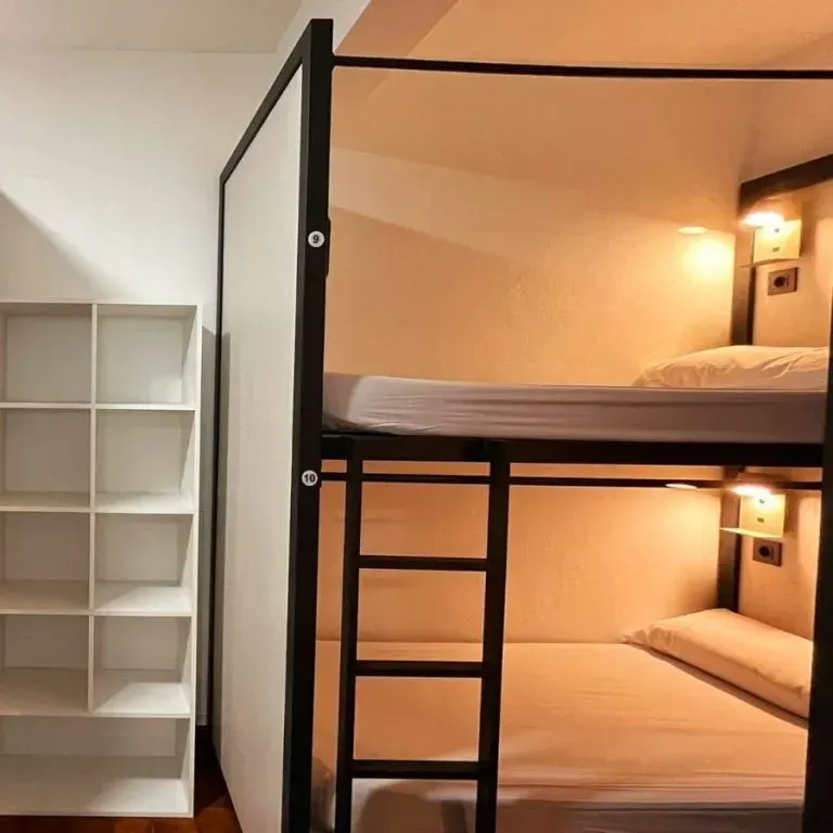 Litera de dos niveles con luces cálidas en una habitación pequeña, junto a una estantería blanca vacía.