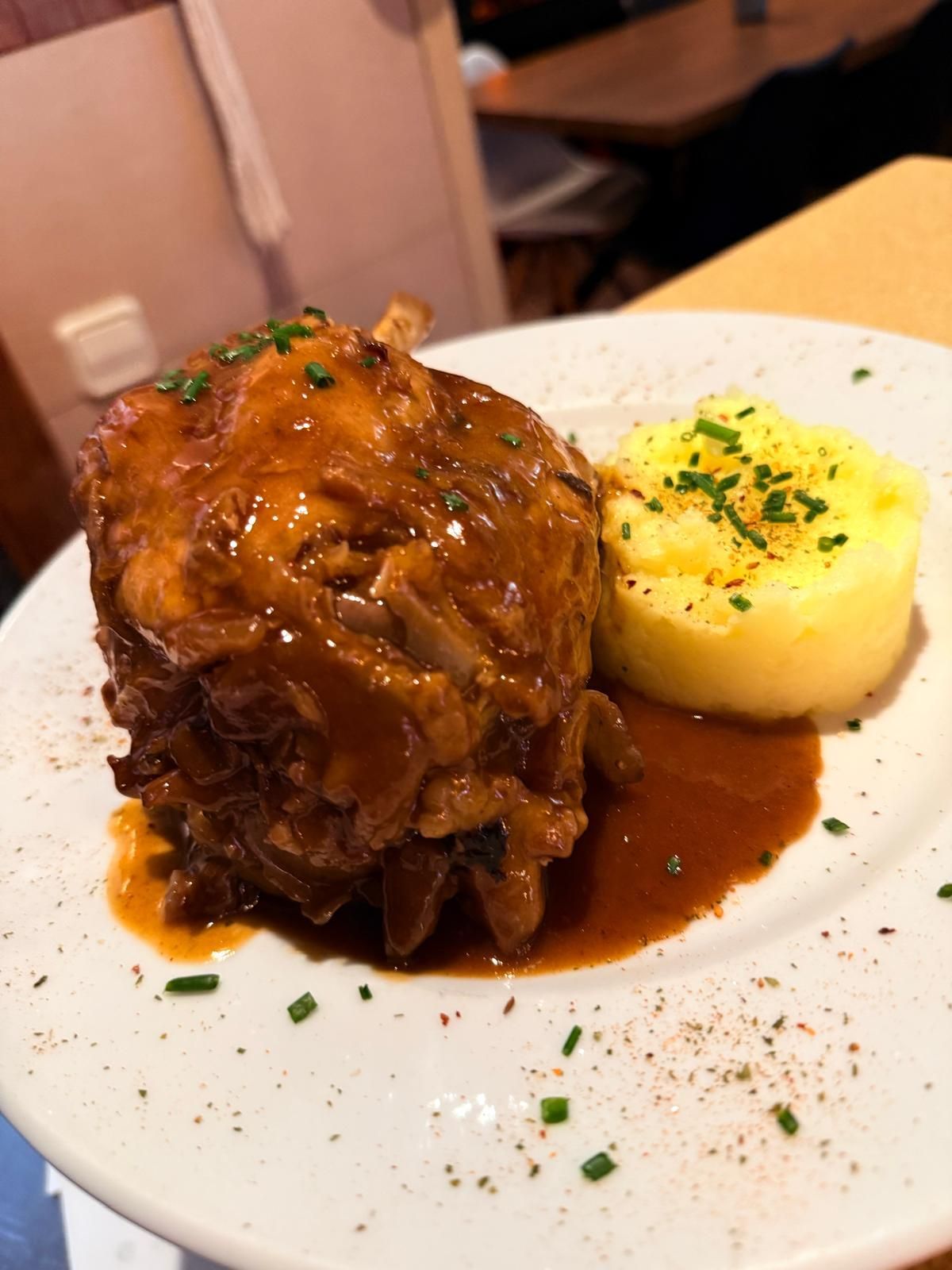 Carne estofada en salsa rica servida con puré de papas en un plato blanco; adornado con cebollino.
