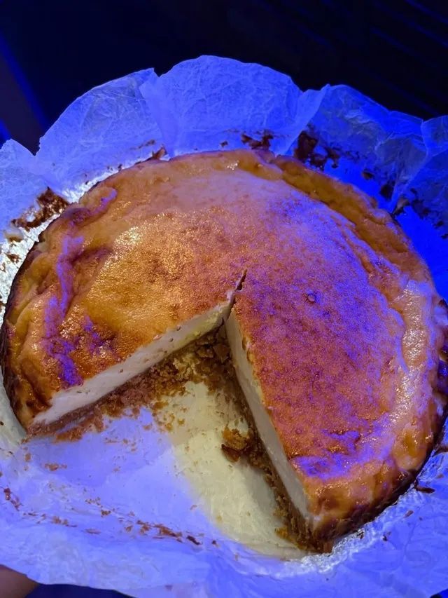 Tarta de queso con una rebanada retirada, sobre papel vegetal blanco. La superficie está dorada y espolvoreada con canela.