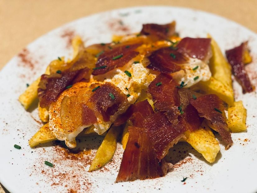 Un plato de patatas fritas cubierto con huevos revueltos, jamón en rodajas finas y pimentón.