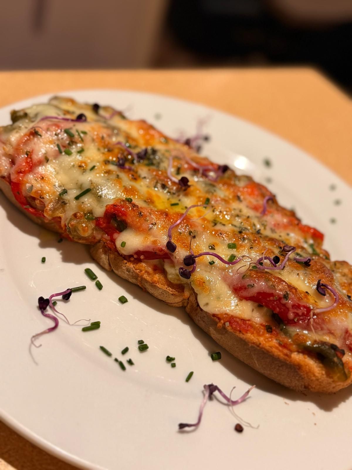 Pan tostado cubierto con queso derretido, pimientos rojos y hierbas, servido en un plato blanco.