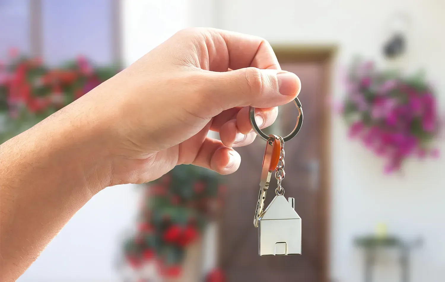 Eine Person hält einen Schlüsselanhänger mit einem Haus vor einem Haus.