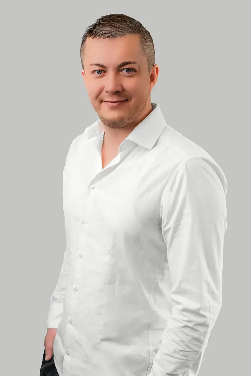Ein Mann in einem weißen Hemd steht vor einem grauen Hintergrund.