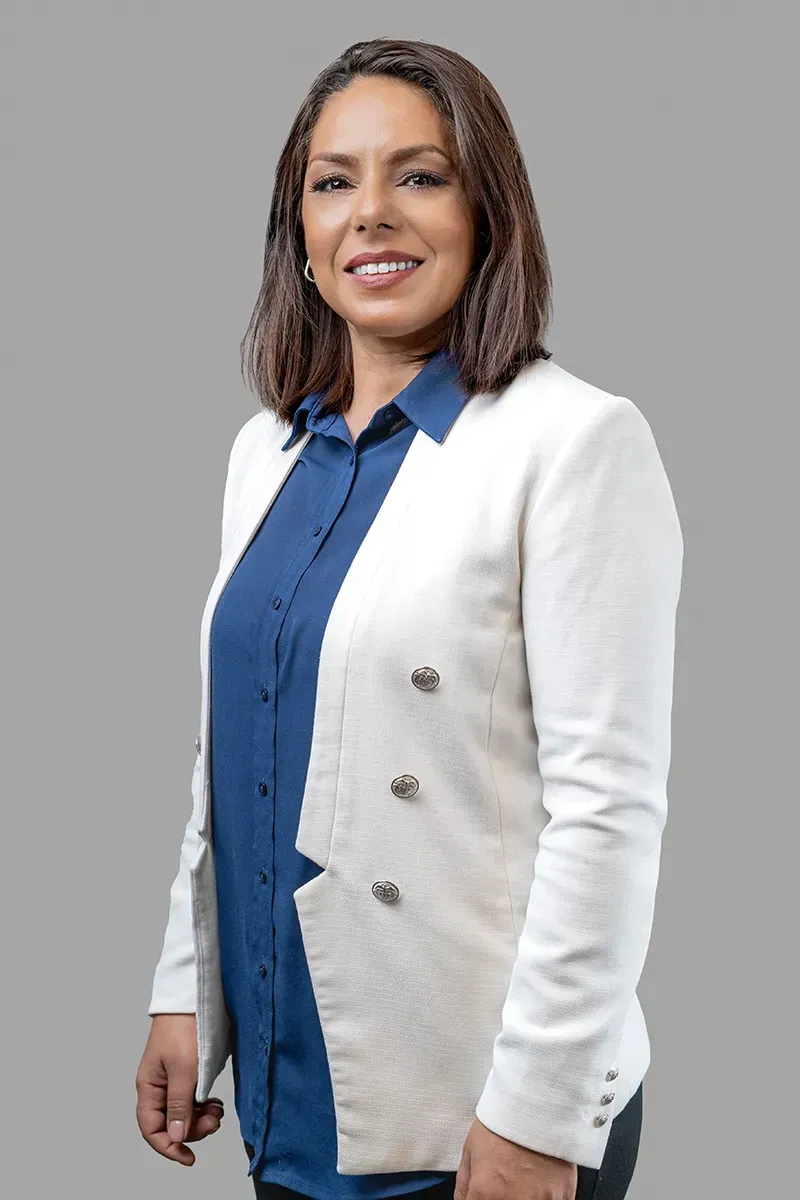 Eine Frau in einer weißen Jacke und einem blauen Hemd lächelt.