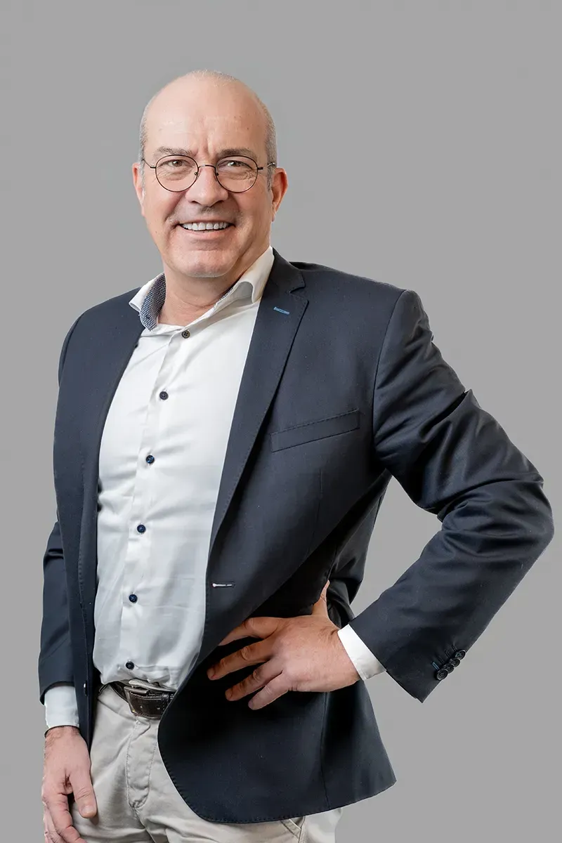 Ein Mann in Anzug und Brille steht mit den Händen in den Hüften da.