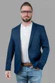 Ein Mann in blauer Jacke und Brille steht mit den Händen in den Taschen da.
