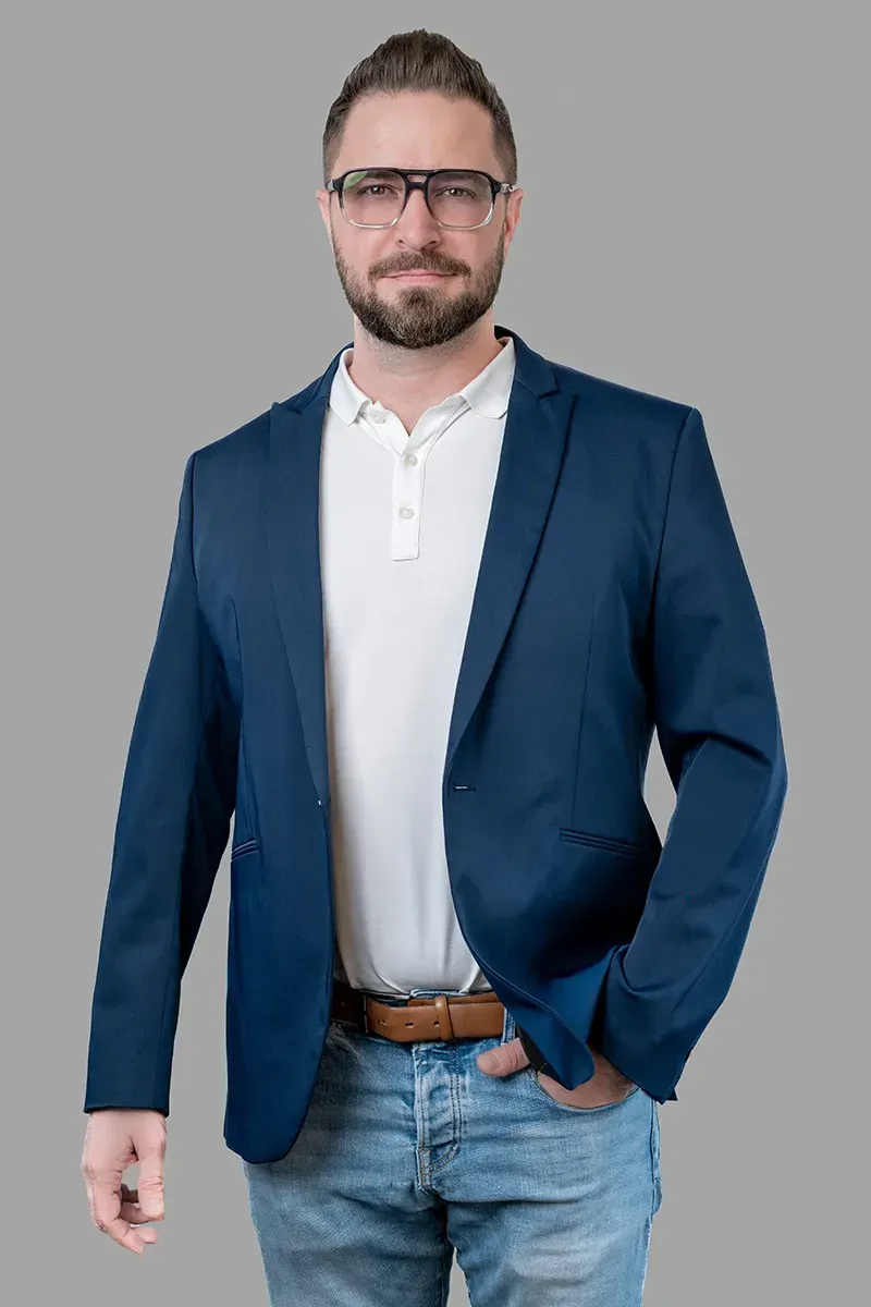 Ein Mann in blauer Jacke und Brille steht mit den Händen in den Taschen da.