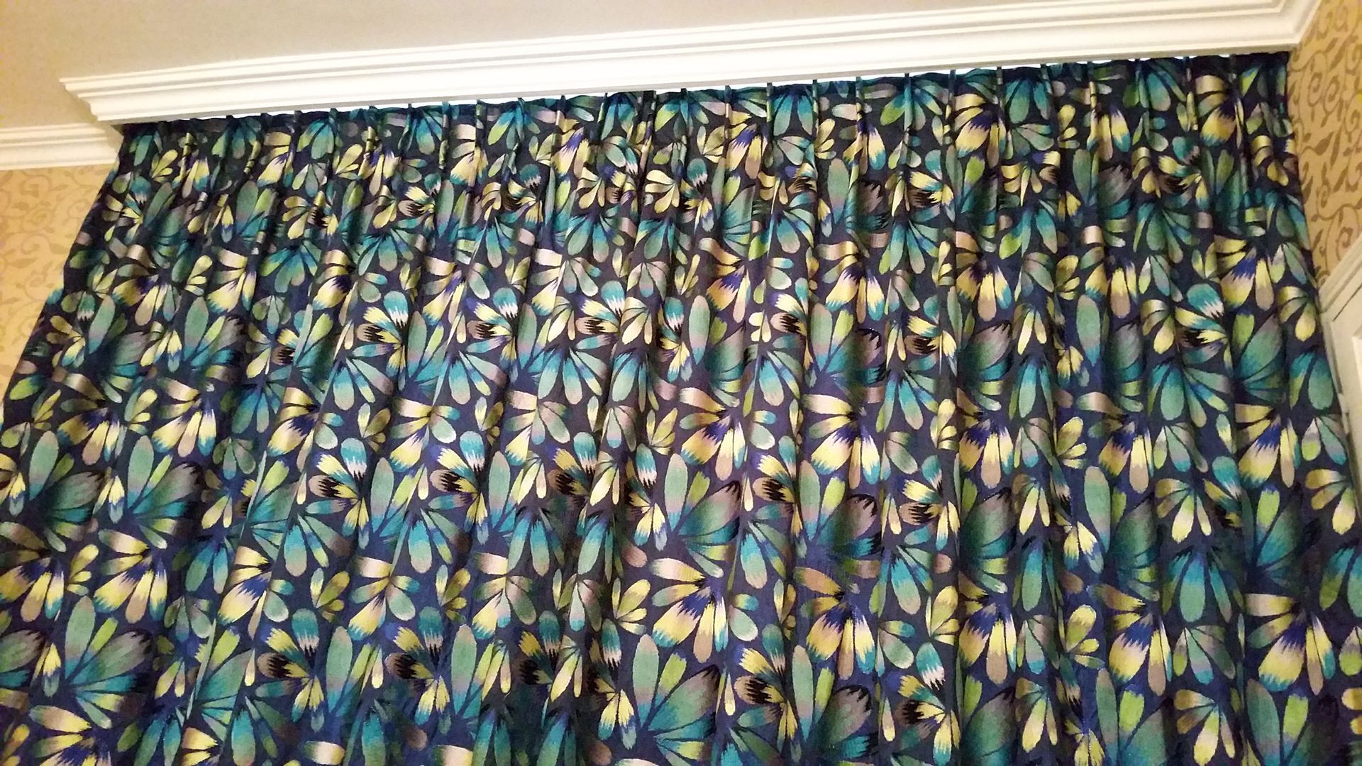 Rideaux à plis piqués , motifs à fleurs  de couleurs bleu foncé bleu clair et dorée dominantes. Moulures visibles au plafond