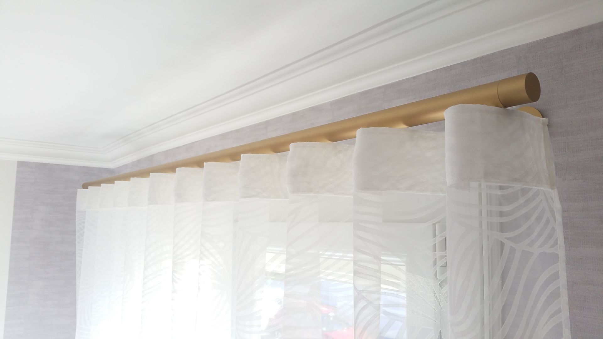 Voilage blanc de grande transparence sur tringle à rideau dorée portée par supports muraux