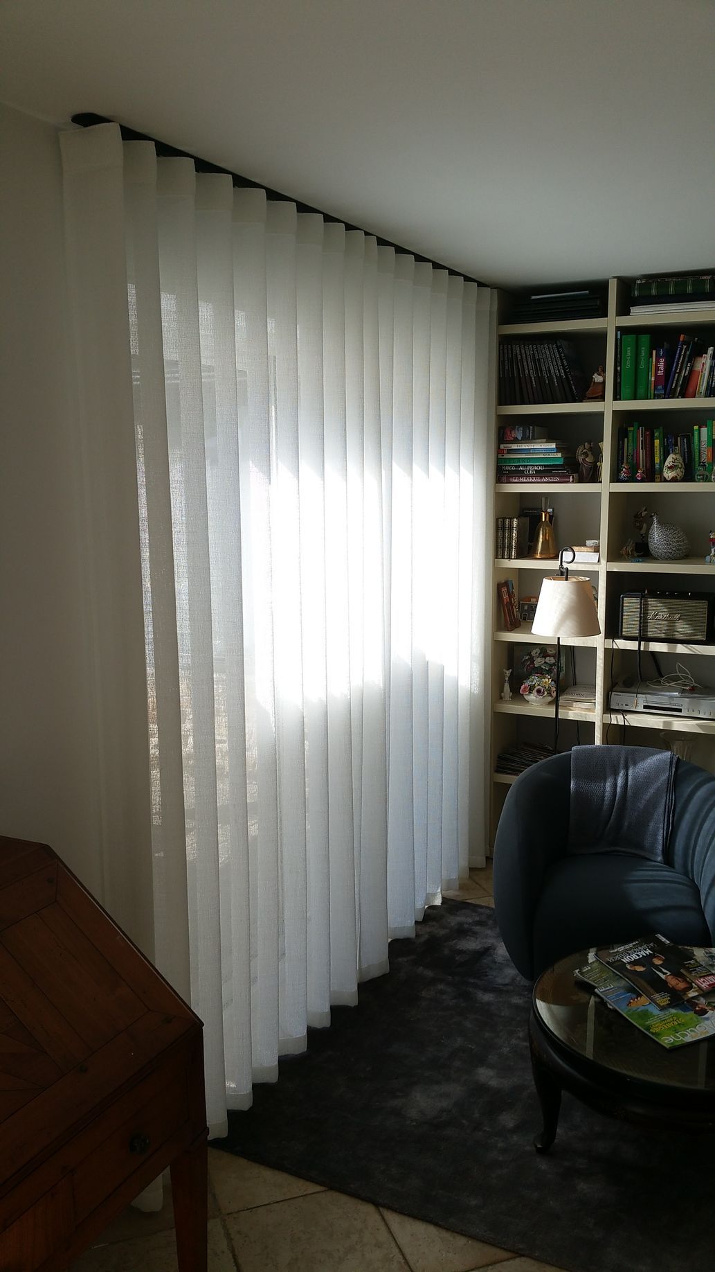 Voilage blanc forme wave avec rail à rideau design noir sur une baie vitrée dans un salon bibliothèque