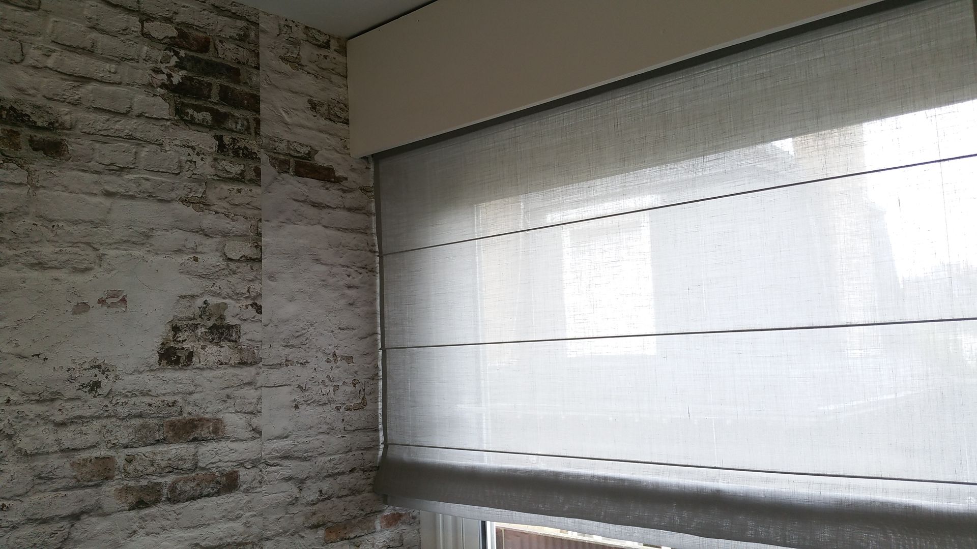 Store avec voilage gris, mur en briques peintes en blanc