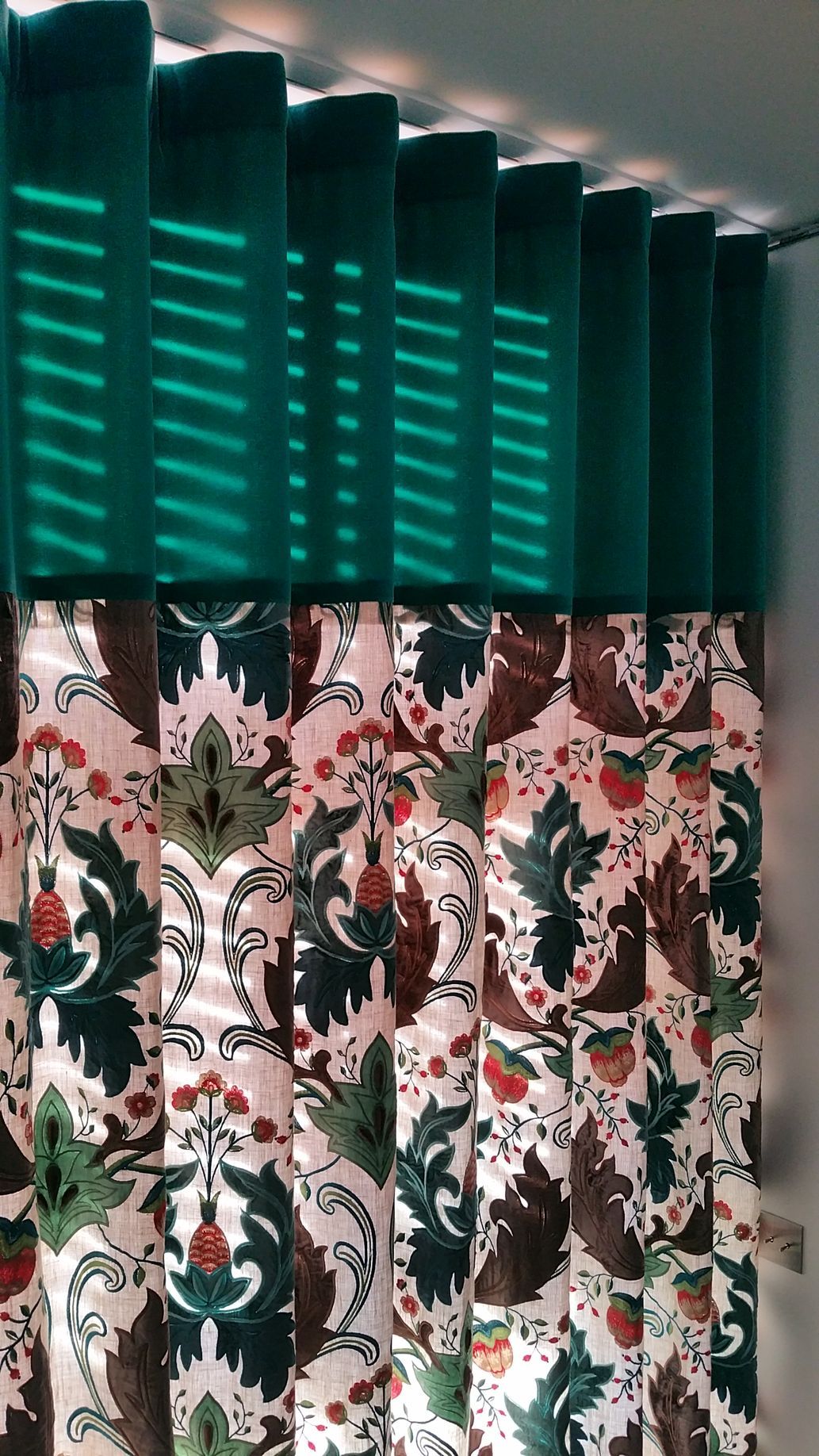 Rideau vert uni en partie supérieure alors que la partie basse montre un décor floral à dominantes verte et rouge sur fond blanc