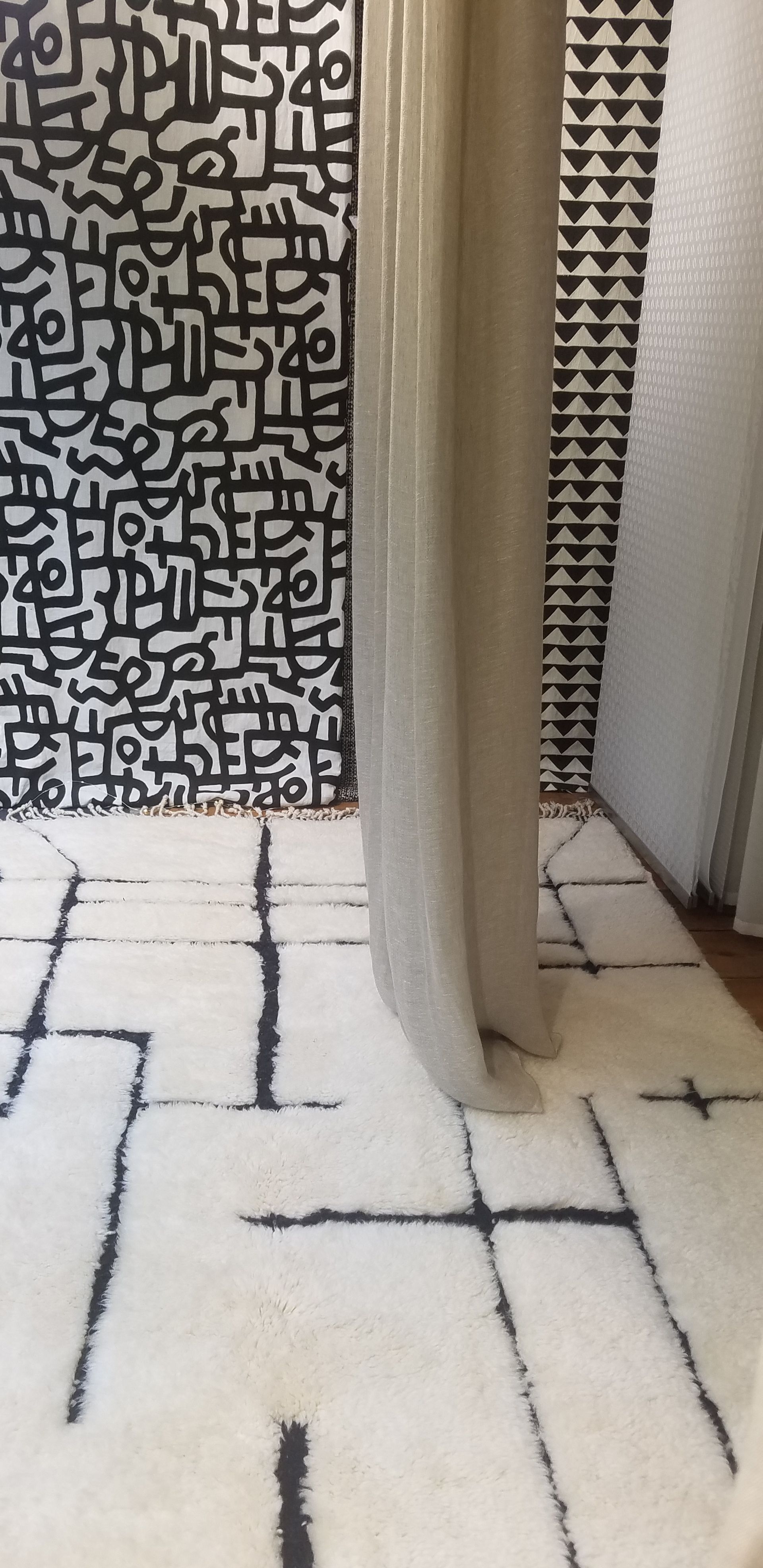 Mise en scène de plusieurs textiles dans notre vitrine de magasin: au sol tapis blanc avec lignes noires, tissus noirs et blancs très graphiques au fond, parois japonaises à droite et rideau au centre retombant sur le tapis