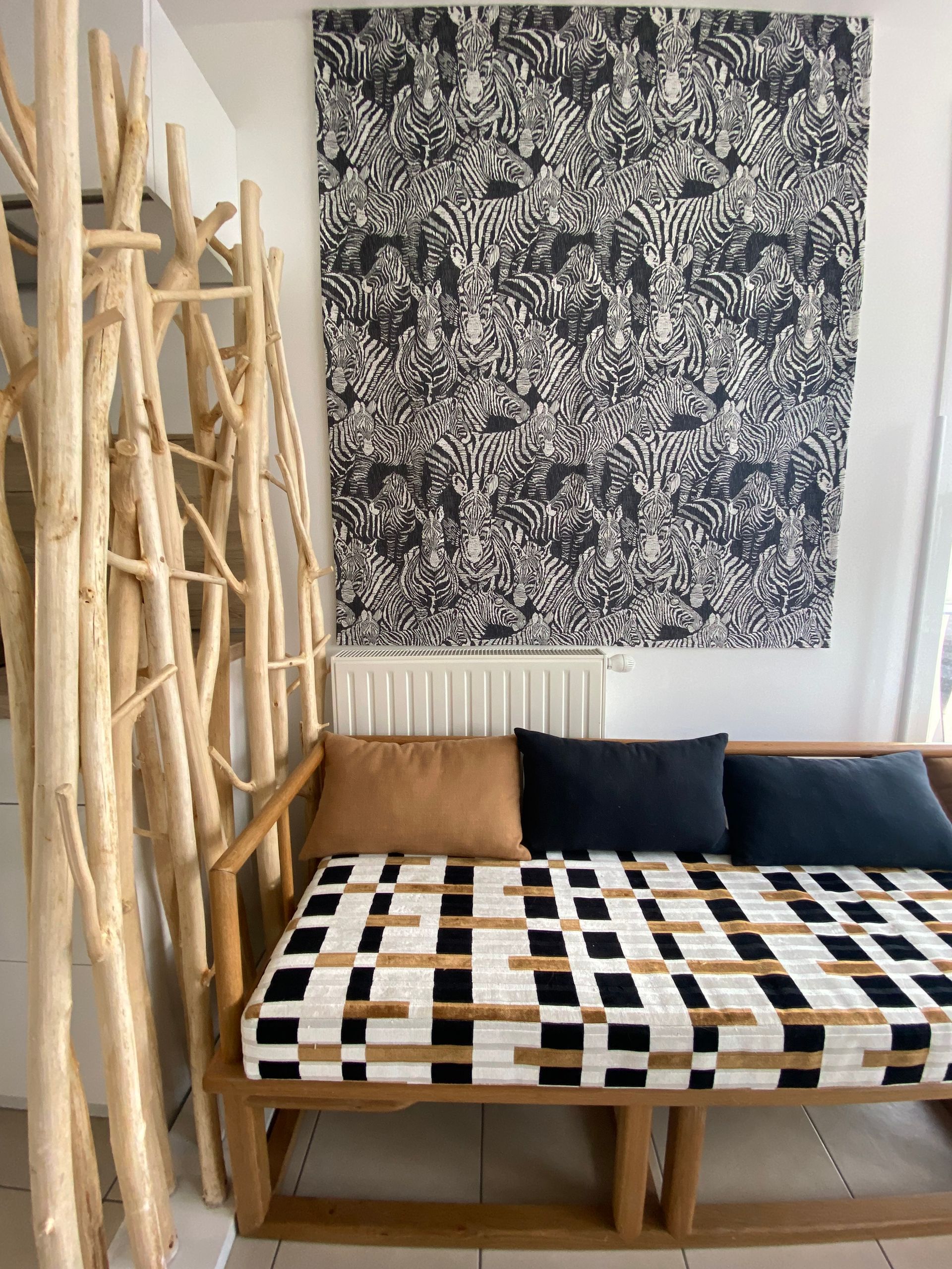 Banquette structure bois et coussins style moderne, décor bois flotté à gauche et tenture tissu noir et blanc avec quantité de zèbres accroché au mur