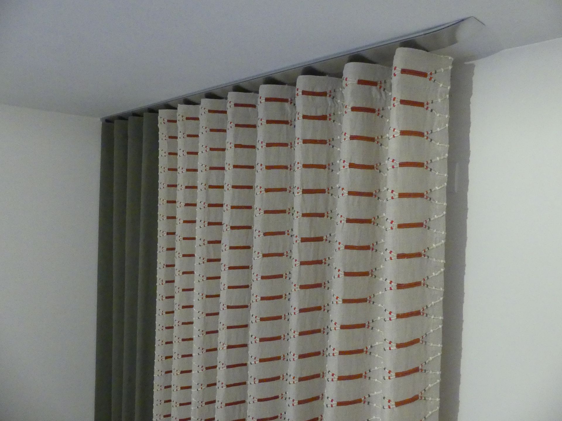 Rideau gris et rideau beige avec motifs orange sur un rail à rideau design finition acier fixé au plafond