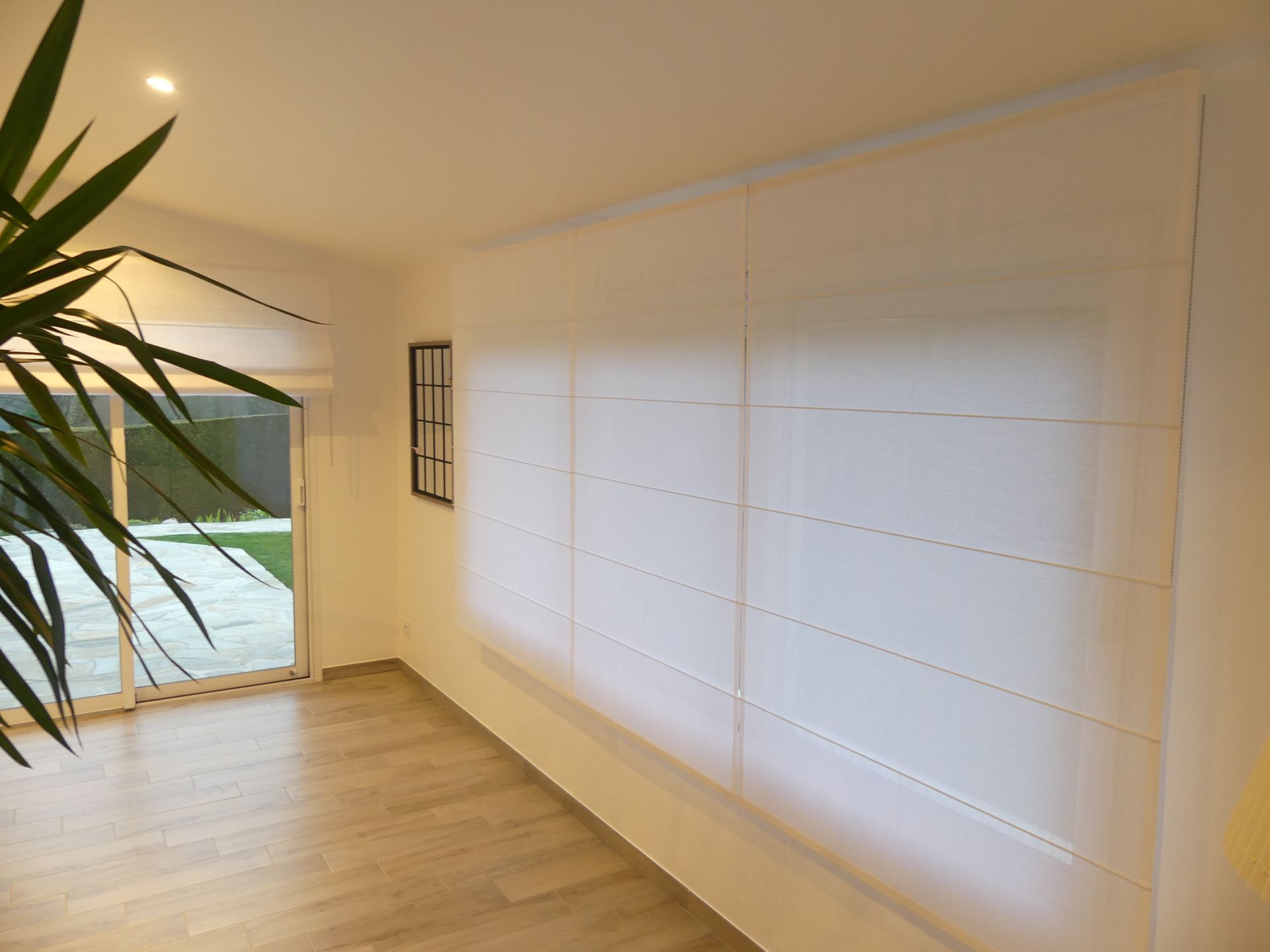 Pièce vide avec baie vitrée et stores bateaux, plante verte au premier plan