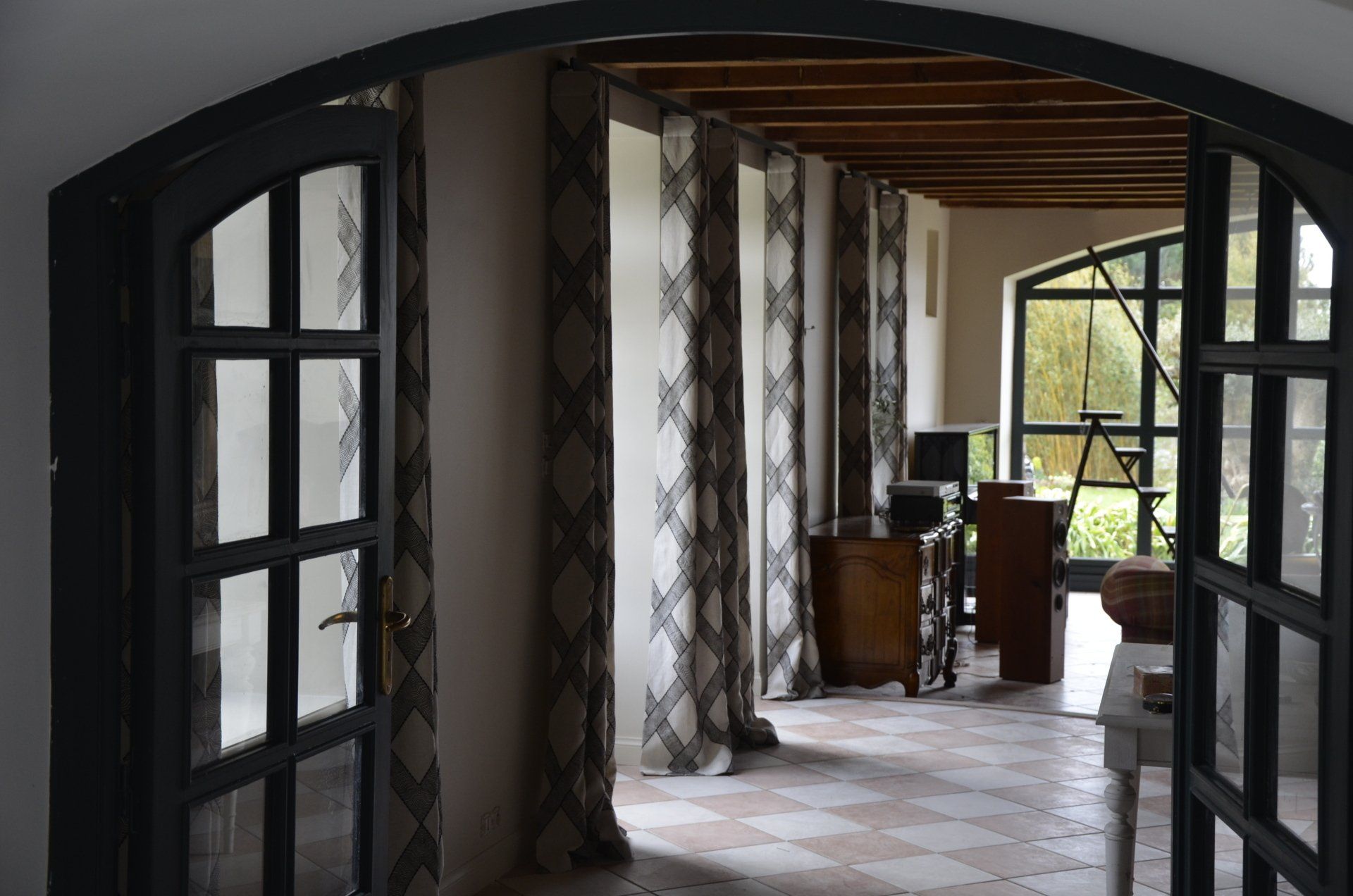 Grande ouverture donnant sur une pièce décorée de rideaux à motifs géométriques sur des rails à rideaux de couleur noire
