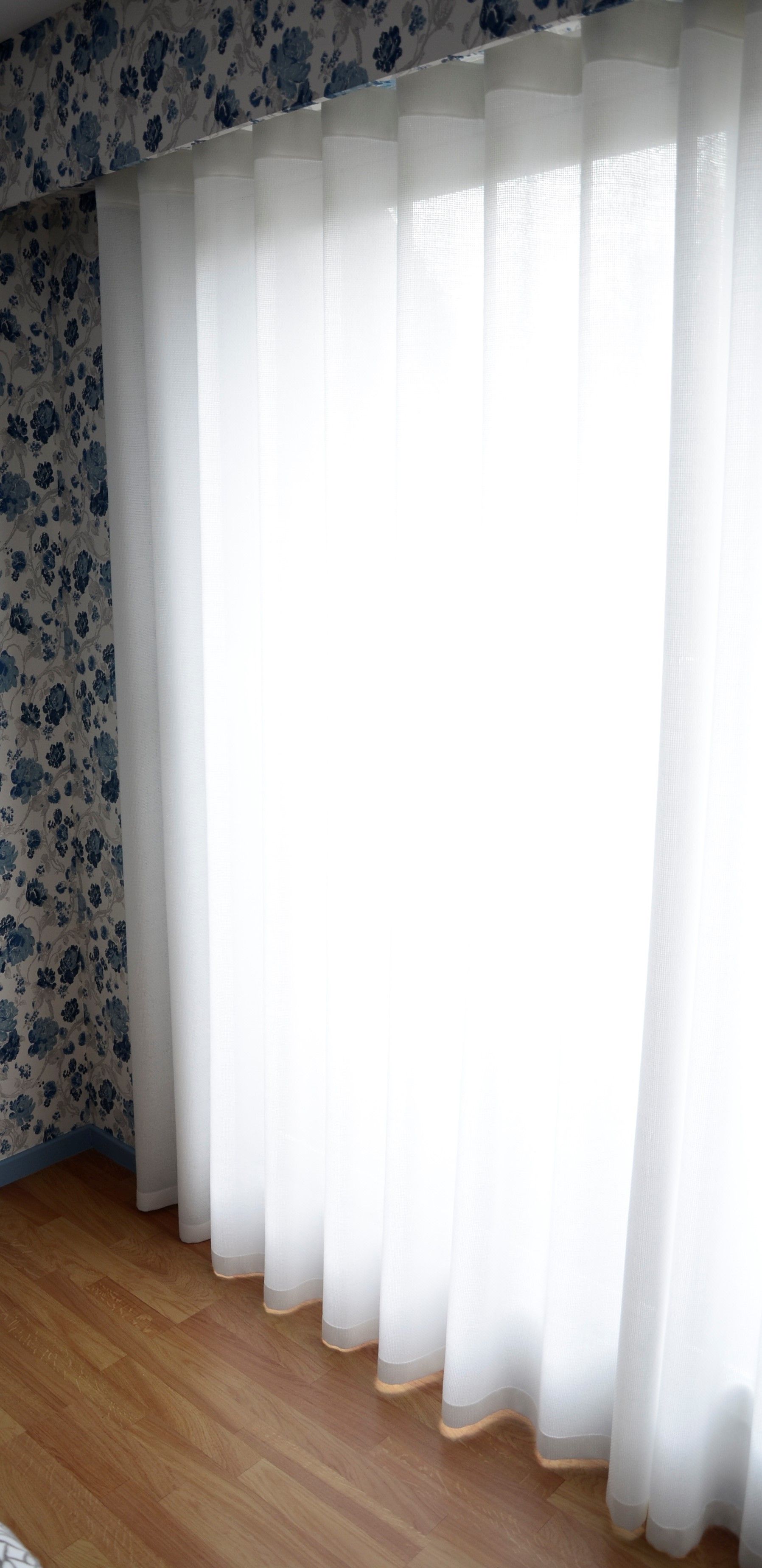 Voilage blanc dans une pièce avec parquet, tapisserie bleue fleurie