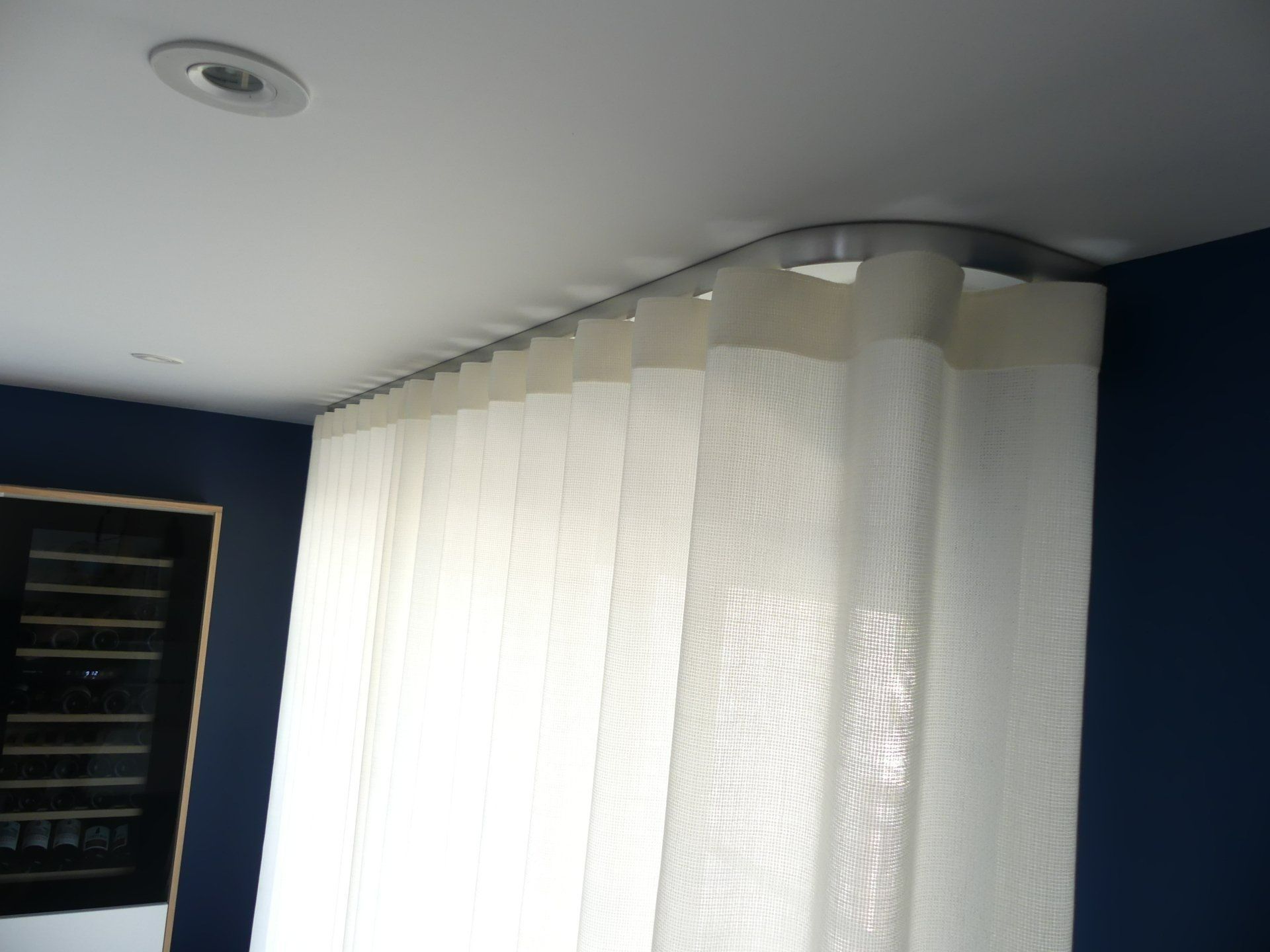 Rideau wave blanc dans une pièce avec des murs peints en bleu marine. Un rail courbe de couleur acier fixé au plafond est utilisé.