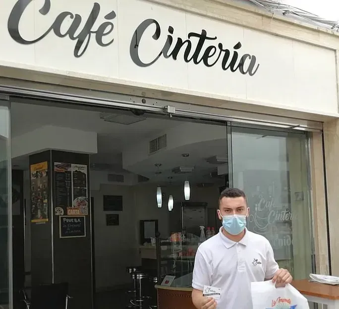 Un hombre con una máscara está parado frente a un café.