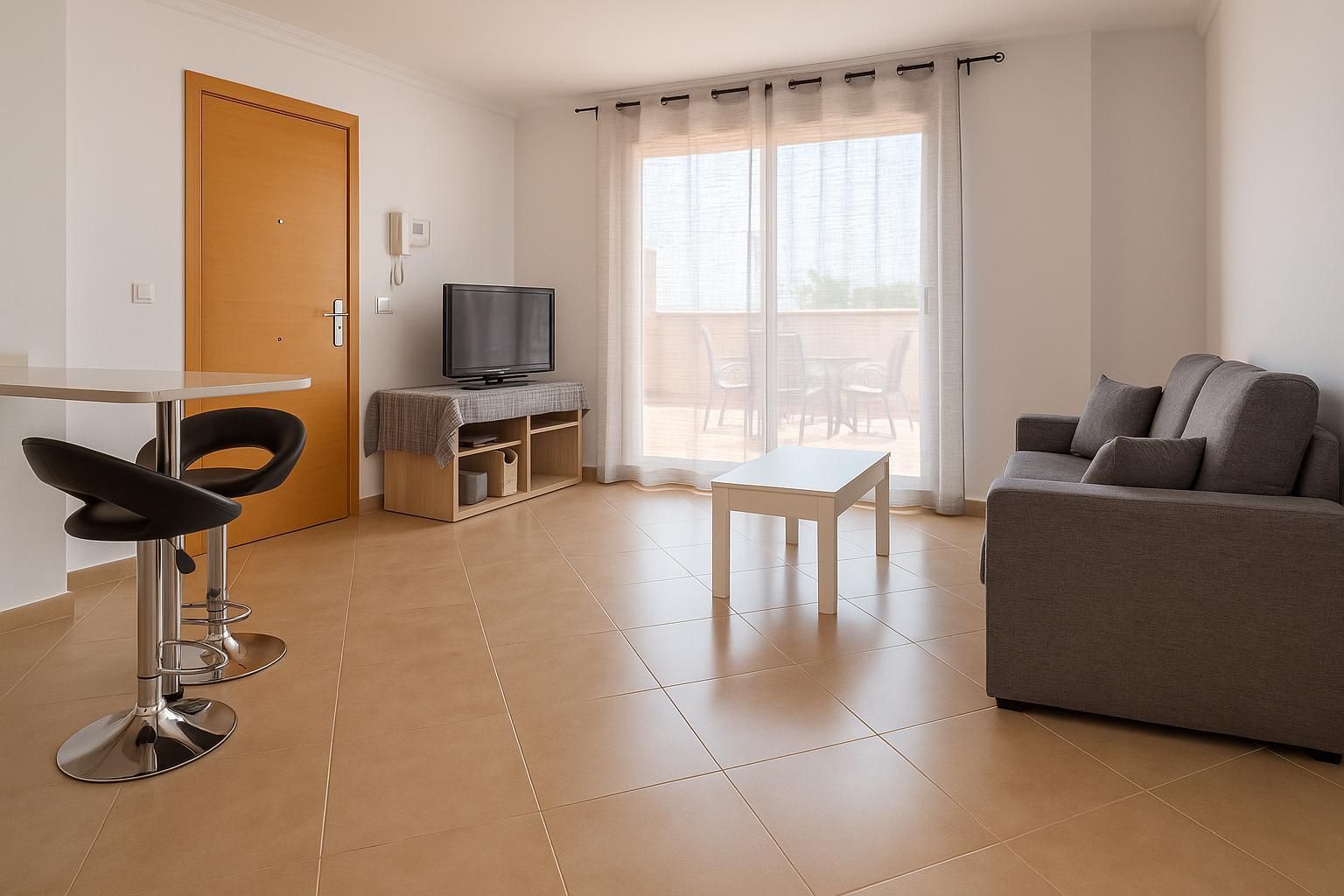 Una pequeña sala de estar con sofá, mesa y televisor. Se ven una puerta y una gran ventana con cortinas transparentes.