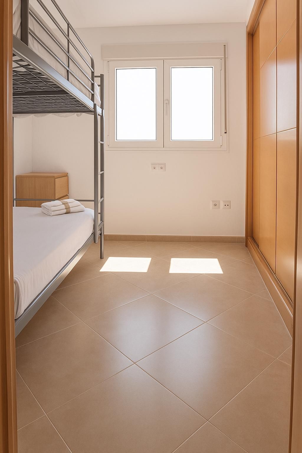 Literas en un dormitorio pequeño con ventana y armario, luz solar en el suelo.