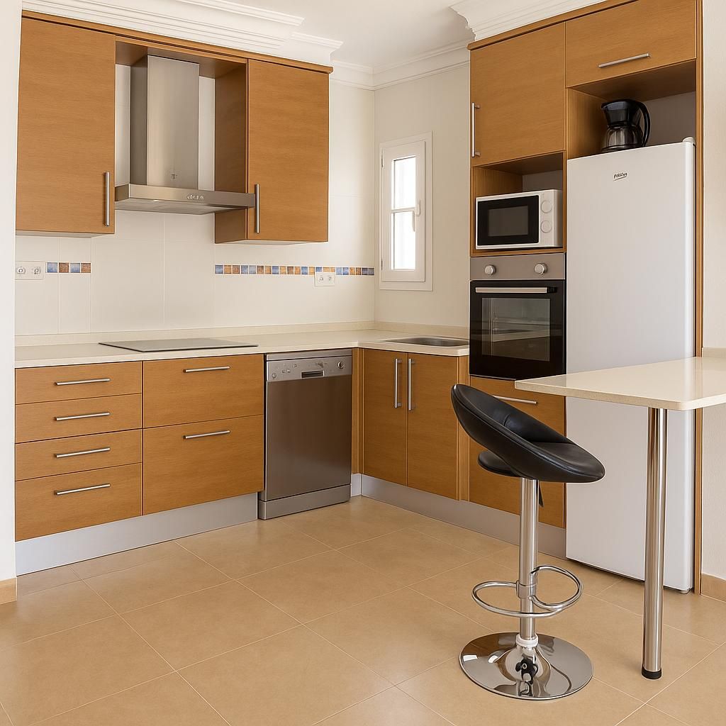 Cocina moderna con gabinetes de madera clara, electrodomésticos de acero inoxidable y una pequeña barra de desayuno.