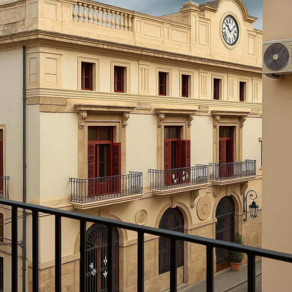Edificio beige con balcones, ventanas arqueadas y torre del reloj.