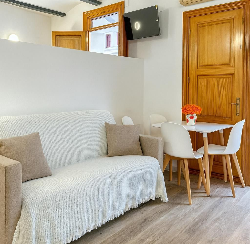 Pequeño espacio de estar con sofá, mesa de comedor y ventana abierta.