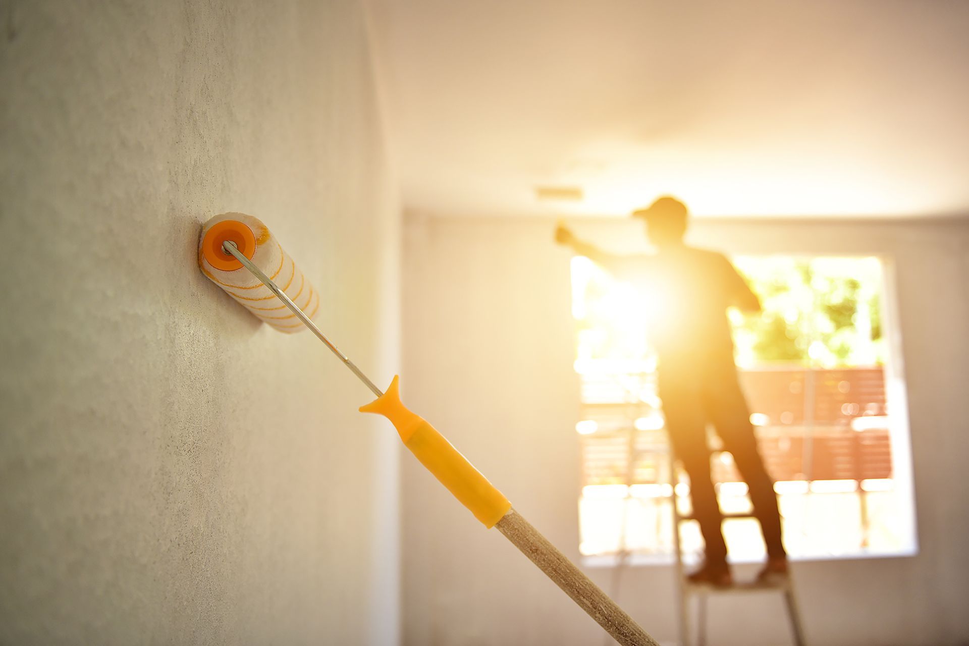 Un homme est debout sur une échelle et peint un mur avec un rouleau à peinture.