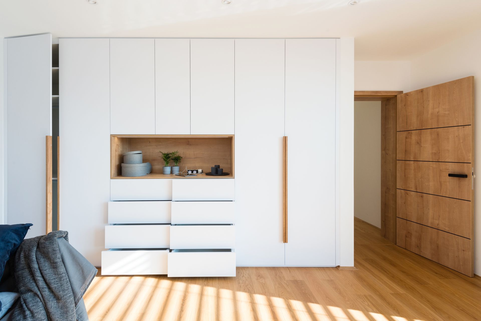 Chambre minimaliste et lumineuse avec armoire blanche, touches de bois et sol rayé de soleil.