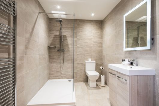 Salle de bains moderne beige avec douche à l'italienne, toilettes et lavabo avec miroir.