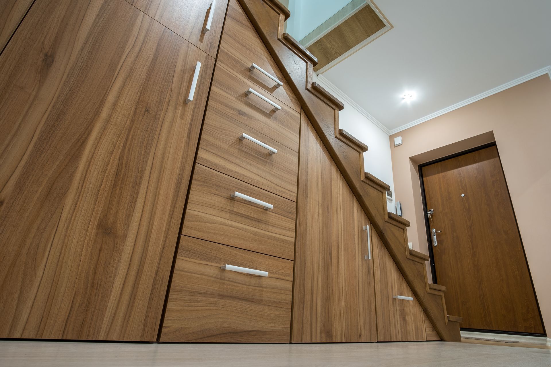Escalier en bois et placards intégrés dans un couloir étroit avec une porte d'entrée.