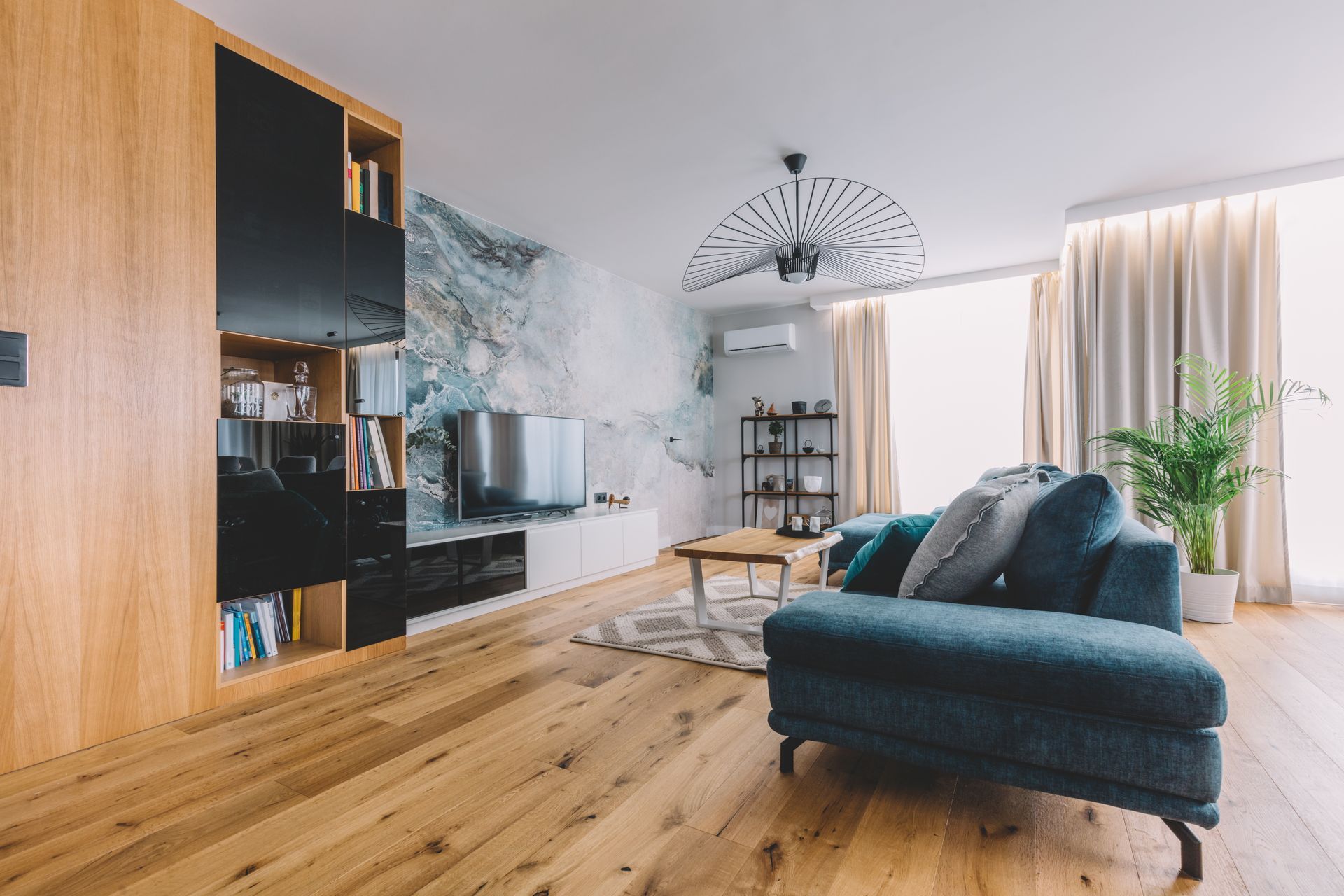 Salon moderne avec parquet, canapé foncé, télévision, cheminée et grandes fenêtres avec rideaux.
