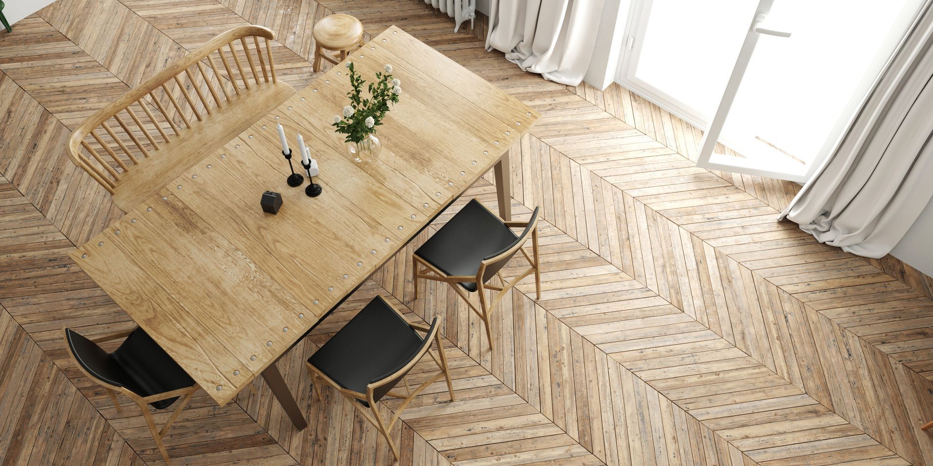 Vue plongeante d'une table à manger avec des chaises noires sur un parquet à chevrons, près de rideaux aux couleurs vives.