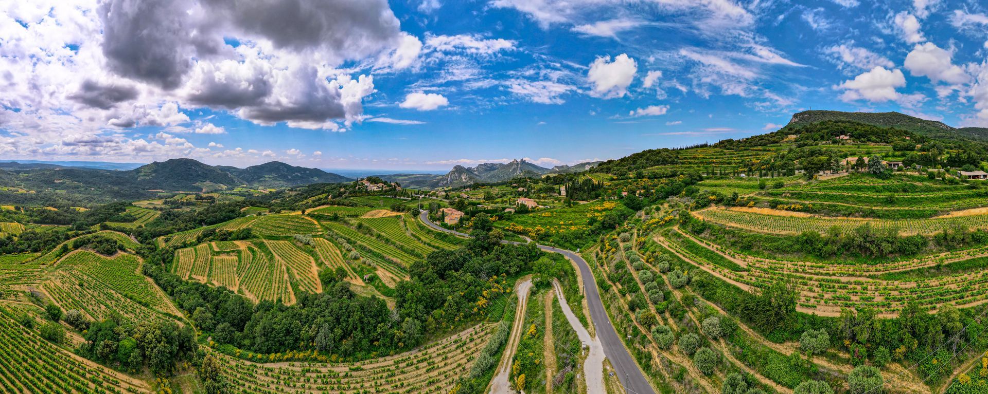 Collines verdoyantes en terrasses et route sinueuse sous un ciel d'un bleu éclatant parsemé de nuages.