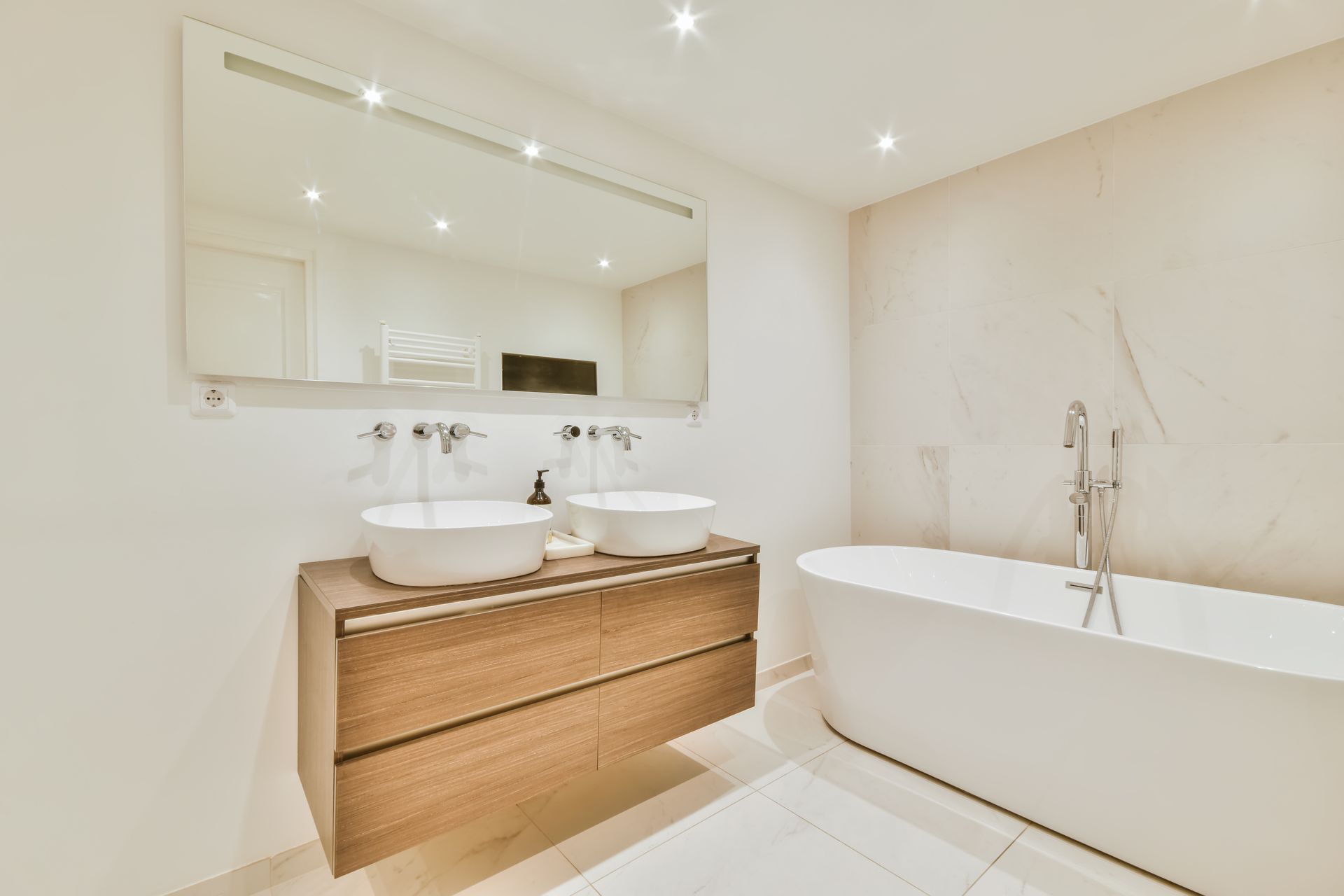 Salle de bains moderne blanche avec double vasque, meuble en bois sous lavabo, grand miroir et baignoire en îlot.
