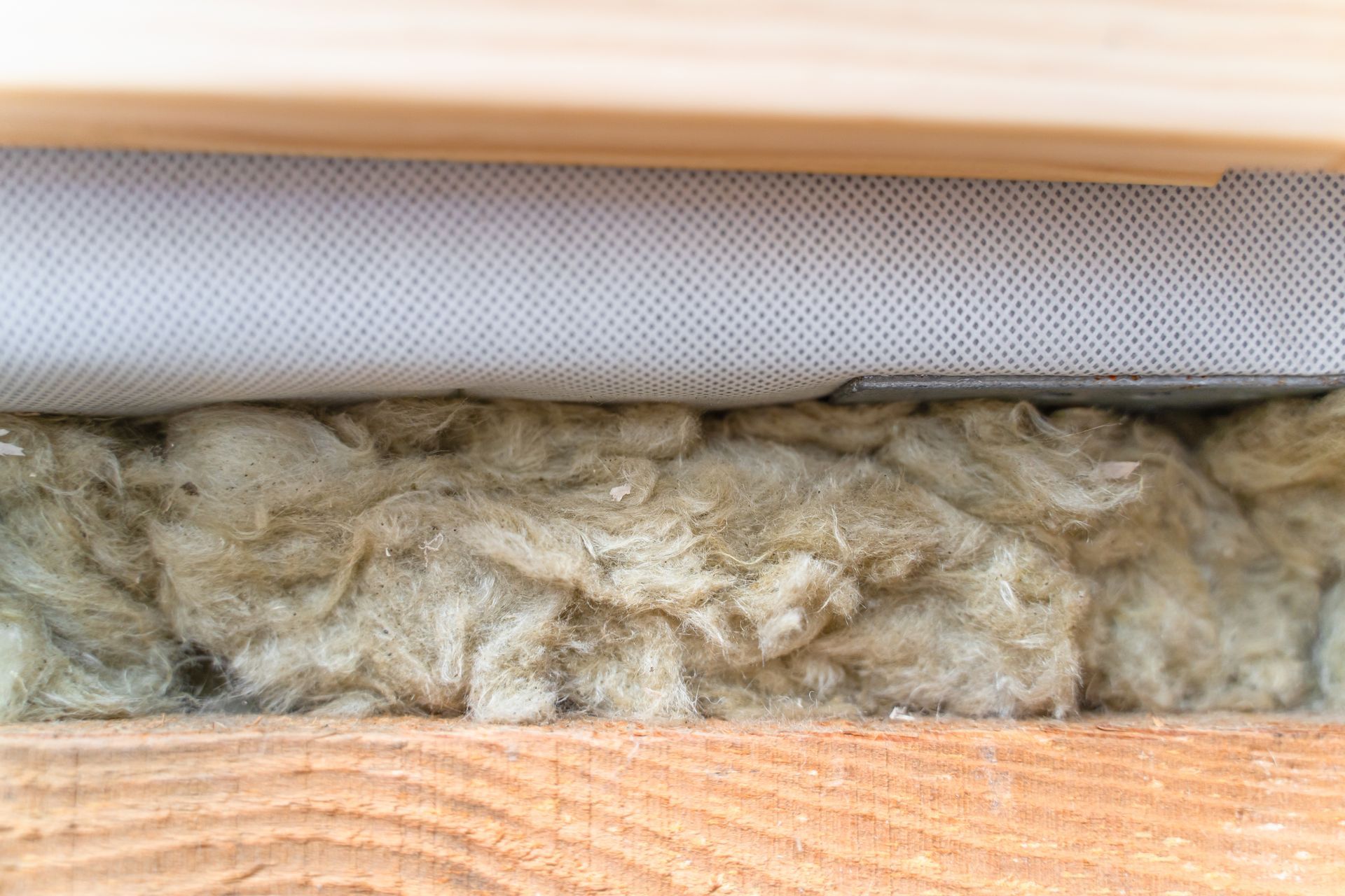 Gros plan sur l'isolant inséré entre une ossature en bois et une couche de treillis blanc.